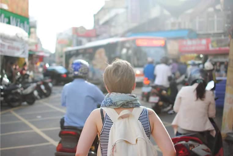 Back view of a solo female traveler walking through a bustling city with a backpack – spontaneous travel tips
