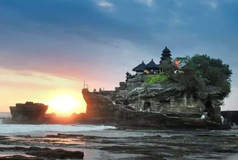 Tanah Lot Bali temple at sunset, surrounded by ocean waves and glowing sky
